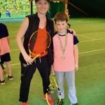Istruttrice tennis e ragazzo con medaglia in campo indoor.