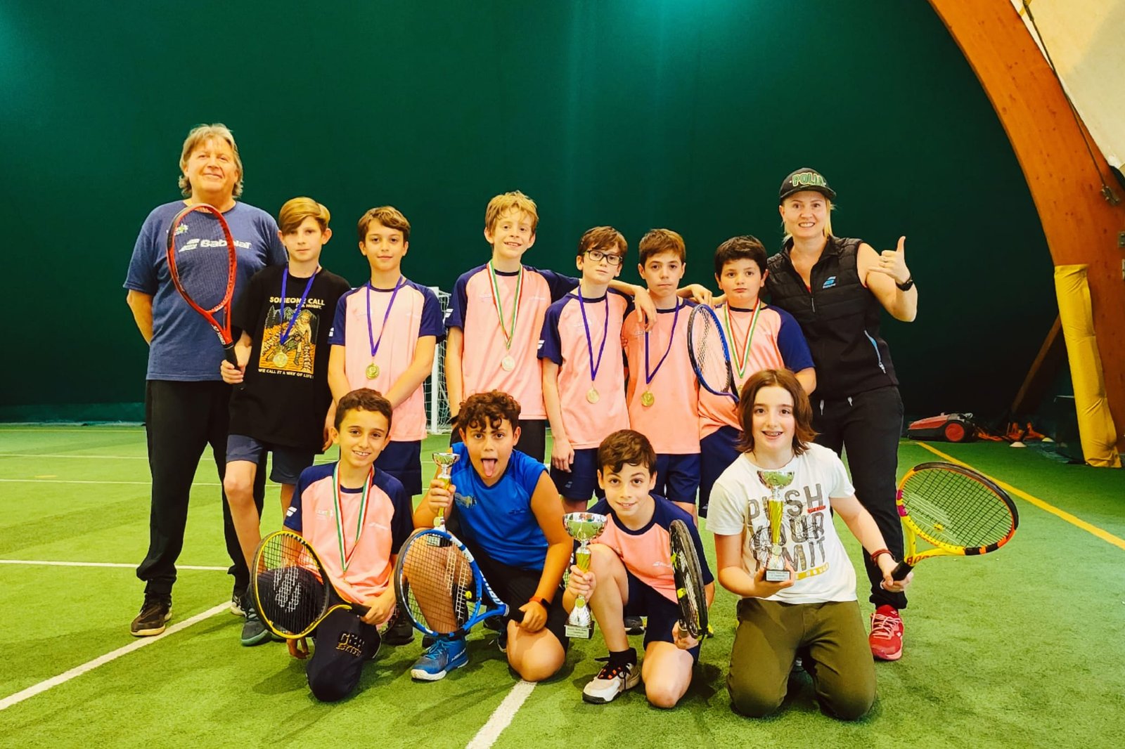 Gruppo giovanile tennisti con trofei e medaglie sul campo.