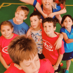 Gruppo di bambini sorridenti con insegnante in palestra.