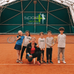 Gruppo di bambini con istruttore su campo da tennis.